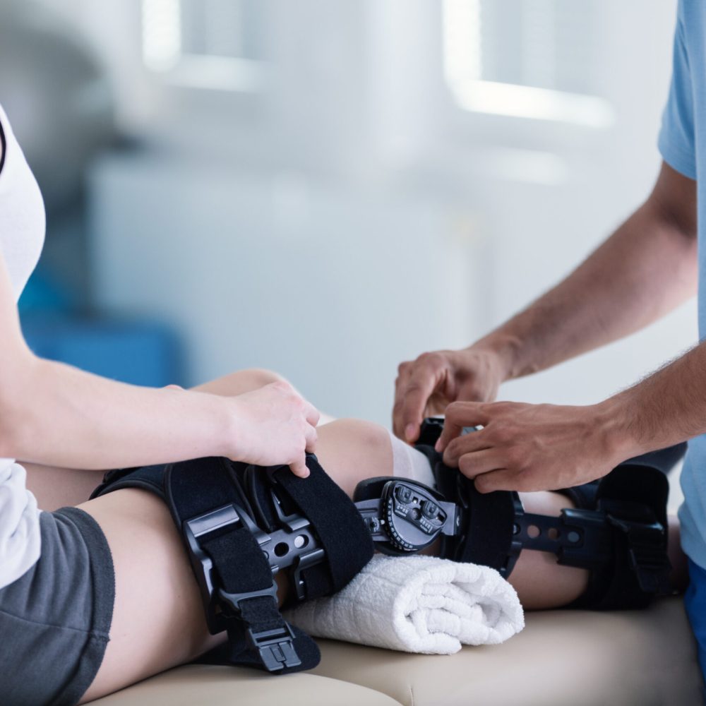 Close-up on person with stiffener on broken leg during rehabilitation with physiotherapist