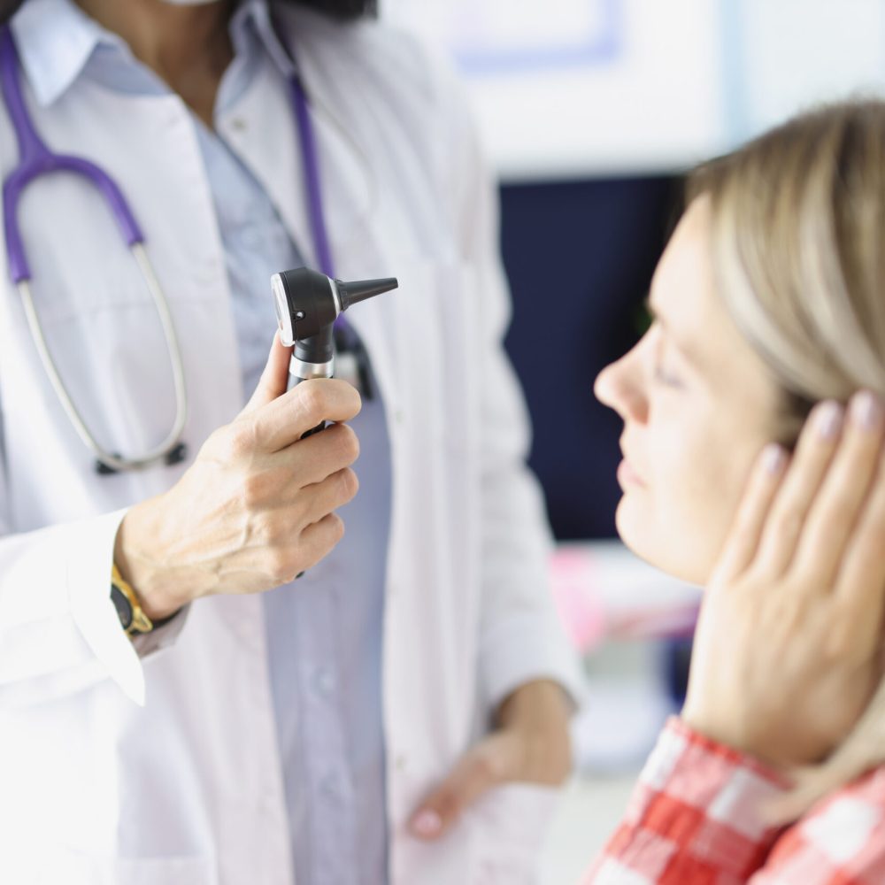 Otorhinolaryngologist examines a woman ear with otoscope. Hearing impairment in adults concept